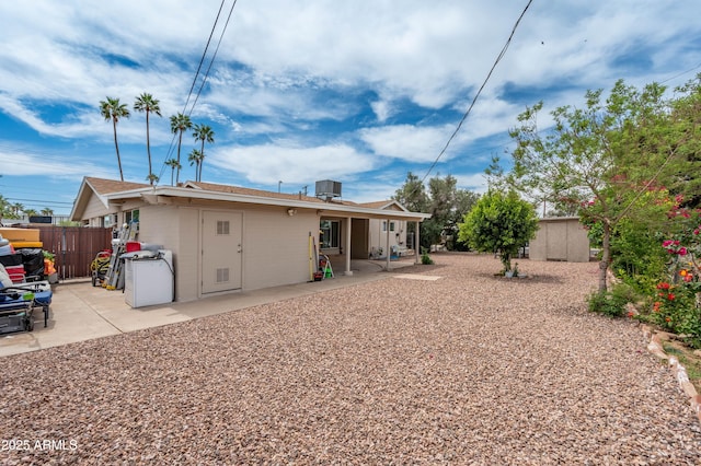 rear view of house with a patio area, central AC unit, concrete block siding, fence, and a shingled roof