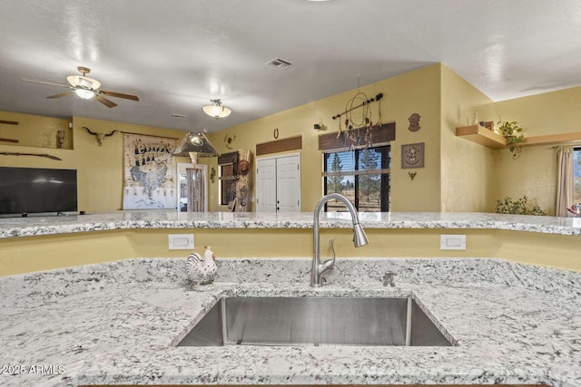 kitchen with a ceiling fan, visible vents, a sink, and light stone countertops