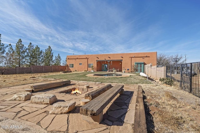 rear view of house with a fenced backyard, a fire pit, and stucco siding