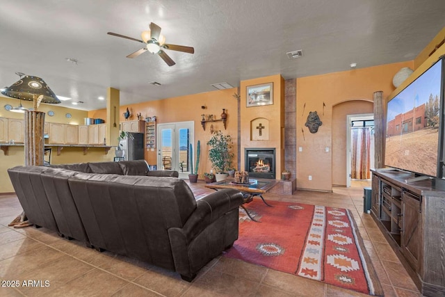 living area featuring a tiled fireplace, tile patterned floors, visible vents, and a ceiling fan