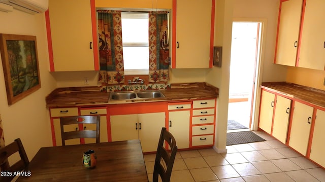 kitchen with white cabinetry, sink, light tile patterned floors, and an AC wall unit