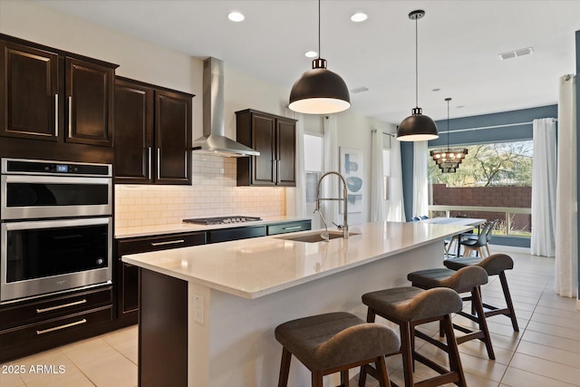 kitchen featuring appliances with stainless steel finishes, sink, a center island with sink, and wall chimney range hood