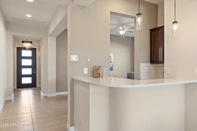 kitchen featuring dark brown cabinetry, tasteful backsplash, kitchen peninsula, light tile patterned floors, and ceiling fan with notable chandelier