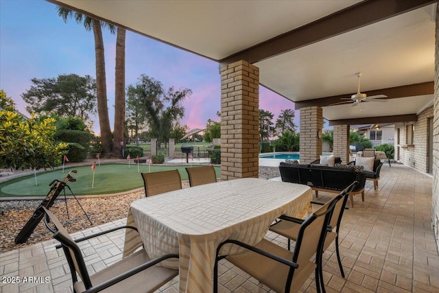 1106 N Villa Nueva Dr, Litchfield Park, AZ 85340 - patio terrace at dusk featuring an area to practice putting, ceiling fan, an outdoor pool, outdoor dining area, and fence