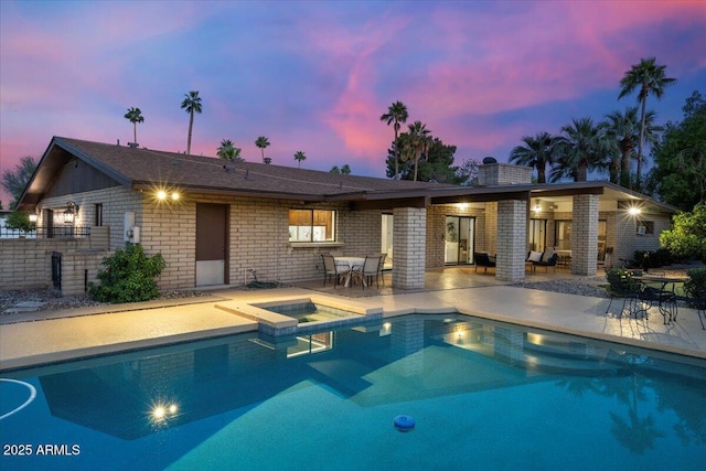 1106 N Villa Nueva Dr, Litchfield Park, AZ 85340 - back of house at dusk with a patio area, brick siding, a pool with connected hot tub, and fence