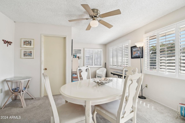 dining space with ceiling fan, light colored carpet, and a textured ceiling