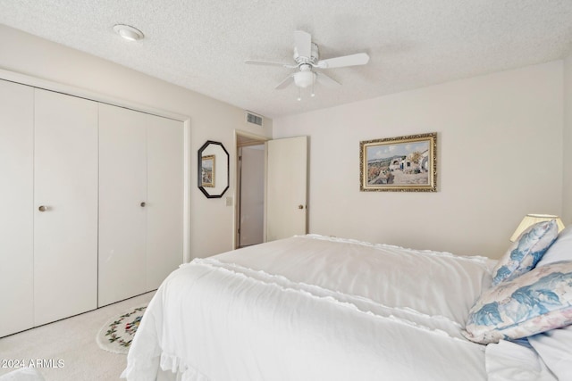 carpeted bedroom with ceiling fan, a closet, and a textured ceiling