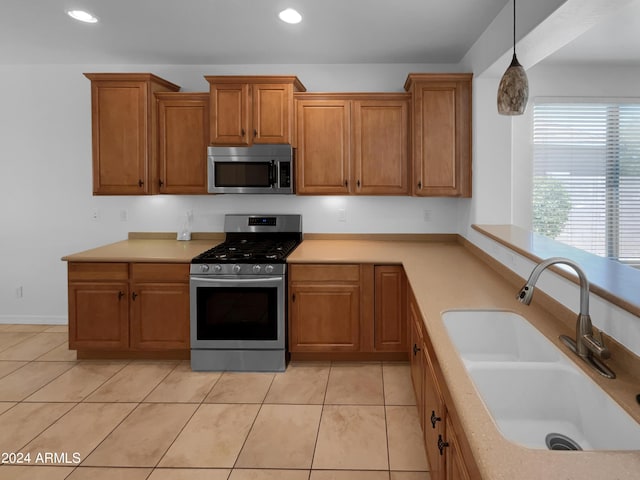 kitchen featuring sink, light tile patterned floors, stainless steel appliances, and decorative light fixtures