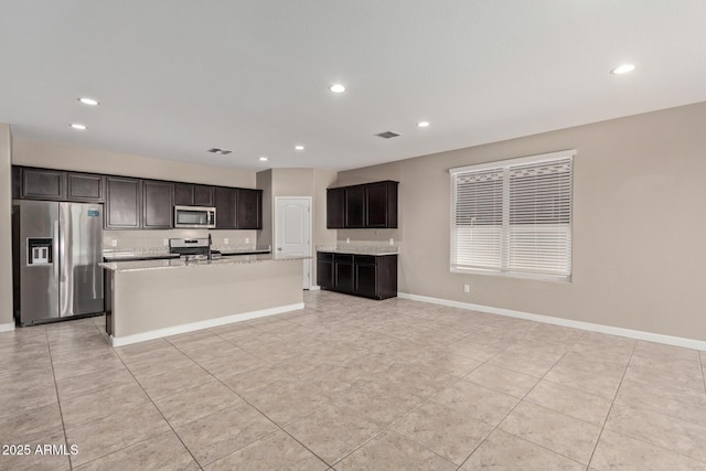 kitchen with dark brown cabinetry, stainless steel appliances, an island with sink, and light tile patterned floors