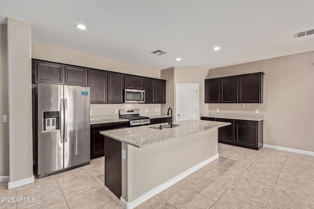 kitchen with sink, stainless steel appliances, dark brown cabinetry, light stone countertops, and an island with sink