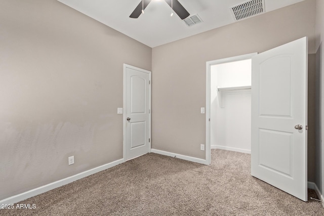 unfurnished bedroom with a spacious closet, a closet, ceiling fan, and carpet flooring