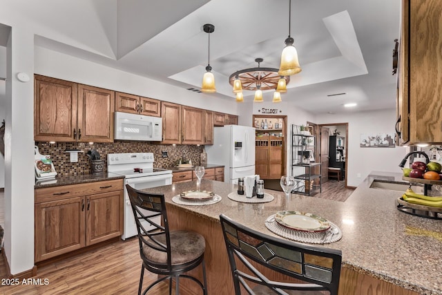 kitchen with decorative backsplash, white appliances, a tray ceiling, and hanging light fixtures