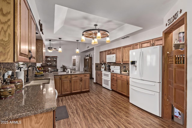 kitchen featuring pendant lighting, kitchen peninsula, sink, a tray ceiling, and white appliances