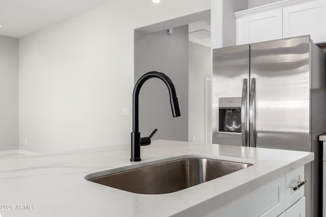 interior space with white cabinetry, sink, light stone countertops, and stainless steel refrigerator with ice dispenser