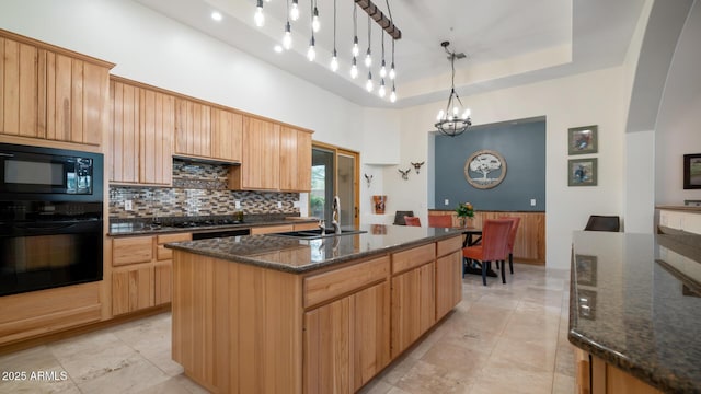 kitchen featuring sink, a raised ceiling, pendant lighting, black appliances, and a kitchen island with sink