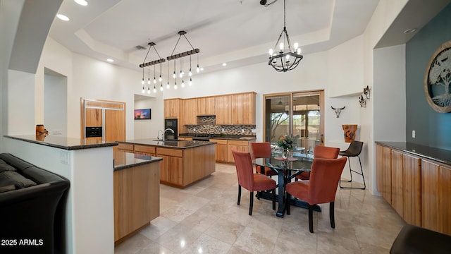 kitchen with a raised ceiling, a notable chandelier, hanging light fixtures, and an island with sink