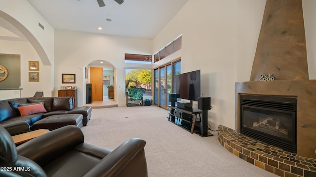 living room with a high ceiling, ceiling fan, carpet, and a large fireplace