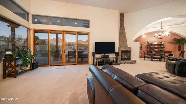 carpeted living room featuring a brick fireplace, an inviting chandelier, and a towering ceiling