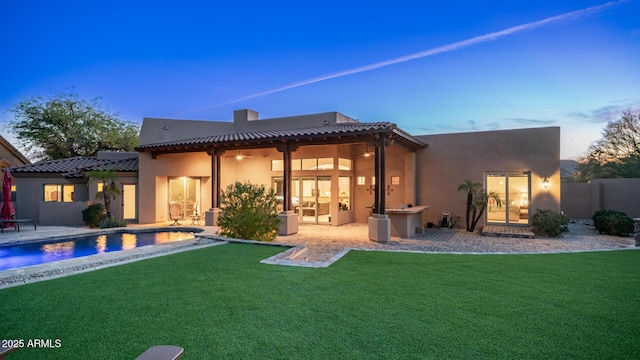 back house at dusk featuring a patio area and a yard