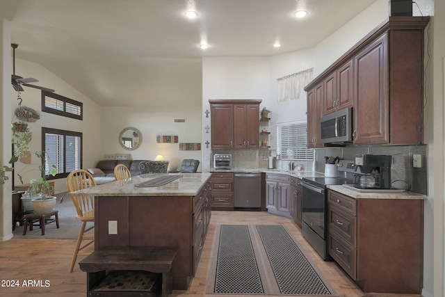 kitchen with light hardwood / wood-style floors, a center island, a kitchen bar, stainless steel appliances, and ceiling fan