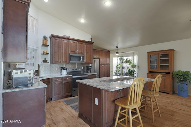 kitchen featuring a kitchen island, light hardwood / wood-style flooring, stainless steel appliances, a breakfast bar, and vaulted ceiling