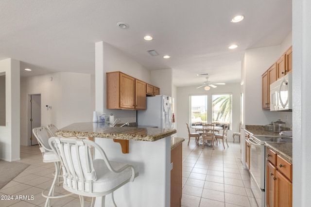 kitchen featuring a breakfast bar, white appliances, kitchen peninsula, light tile patterned floors, and ceiling fan