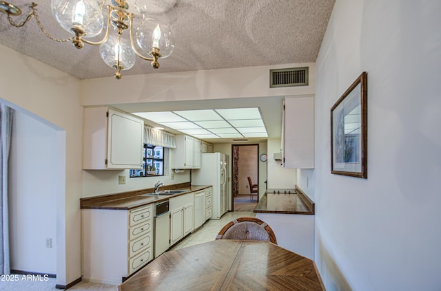 kitchen with white appliances, visible vents, a sink, dark countertops, and a notable chandelier