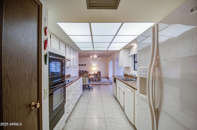 kitchen with black appliances, a sink, dark countertops, light tile patterned floors, and a paneled ceiling