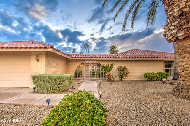 mediterranean / spanish-style home with a tiled roof, an attached garage, and brick siding