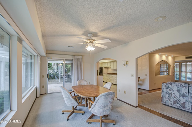 dining space featuring arched walkways, light colored carpet, a healthy amount of sunlight, and a ceiling fan