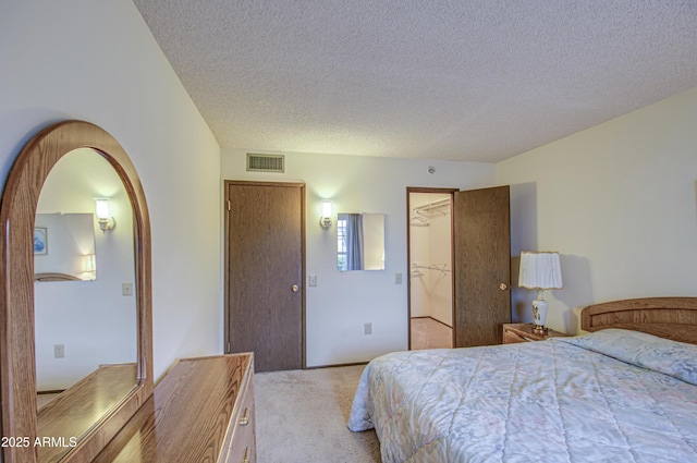 carpeted bedroom with visible vents, arched walkways, a closet, a textured ceiling, and a walk in closet