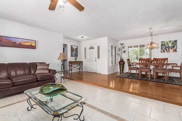 living room featuring light tile patterned floors, ceiling fan with notable chandelier, and a textured ceiling