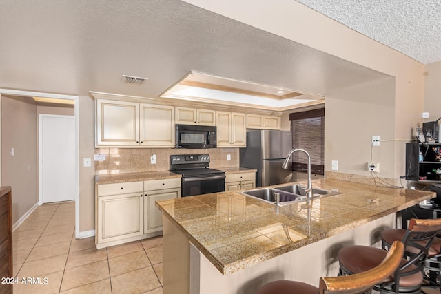 kitchen featuring black appliances, sink, kitchen peninsula, a raised ceiling, and a breakfast bar