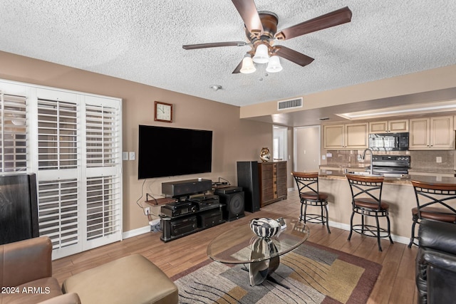 living room with a textured ceiling, ceiling fan, and light hardwood / wood-style flooring