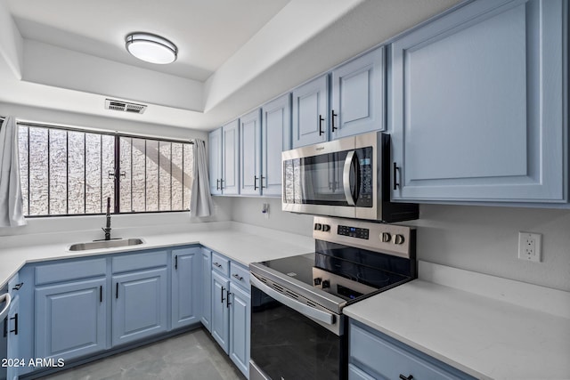 kitchen with appliances with stainless steel finishes, blue cabinetry, sink, and a tray ceiling