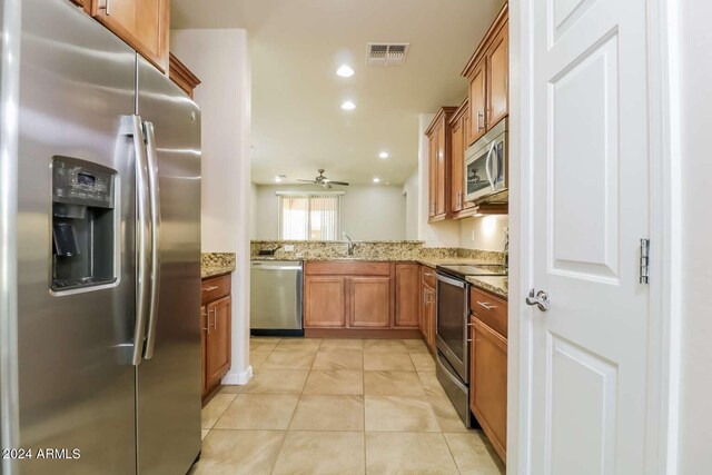 kitchen with stainless steel appliances, kitchen peninsula, light stone counters, sink, and ceiling fan