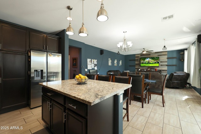 kitchen featuring a center island, stainless steel refrigerator with ice dispenser, hanging light fixtures, dark brown cabinets, and a breakfast bar area