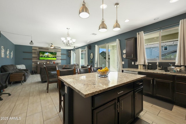 kitchen with a kitchen island, pendant lighting, ceiling fan with notable chandelier, light stone counters, and dark brown cabinetry