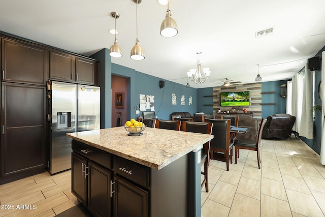 kitchen featuring pendant lighting, dark brown cabinetry, a kitchen island, stainless steel refrigerator with ice dispenser, and a breakfast bar area