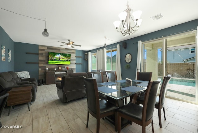 dining space featuring a fireplace and ceiling fan with notable chandelier