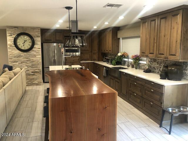 kitchen with sink, a kitchen island, backsplash, pendant lighting, and appliances with stainless steel finishes