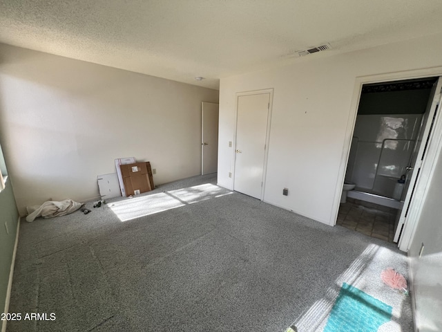 unfurnished bedroom with carpet, a textured ceiling, and ensuite bath