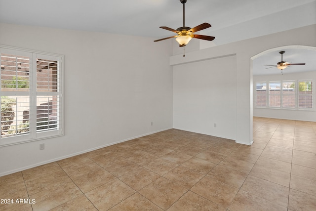 tiled empty room with vaulted ceiling, ceiling fan, and plenty of natural light