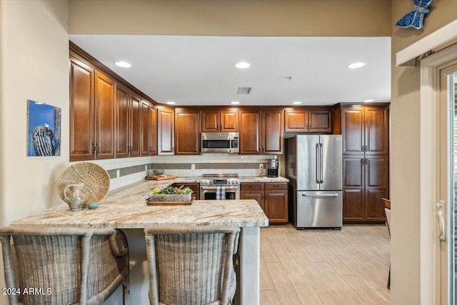 kitchen with kitchen peninsula, stainless steel appliances, light wood-type flooring, a kitchen bar, and decorative backsplash