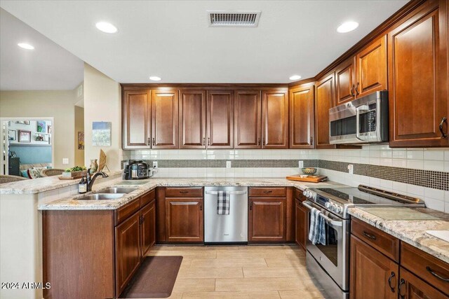 kitchen featuring sink, kitchen peninsula, backsplash, appliances with stainless steel finishes, and light stone countertops