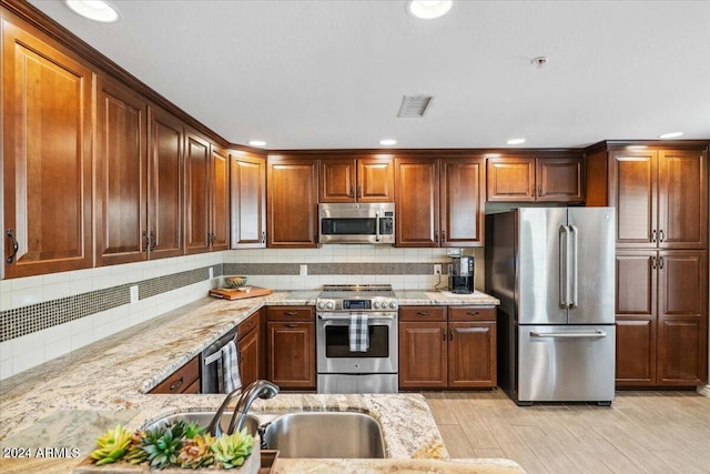 kitchen featuring light wood-type flooring, light stone counters, sink, backsplash, and appliances with stainless steel finishes