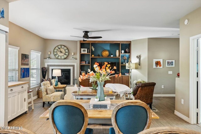 dining area featuring ceiling fan, a tiled fireplace, and light hardwood / wood-style floors