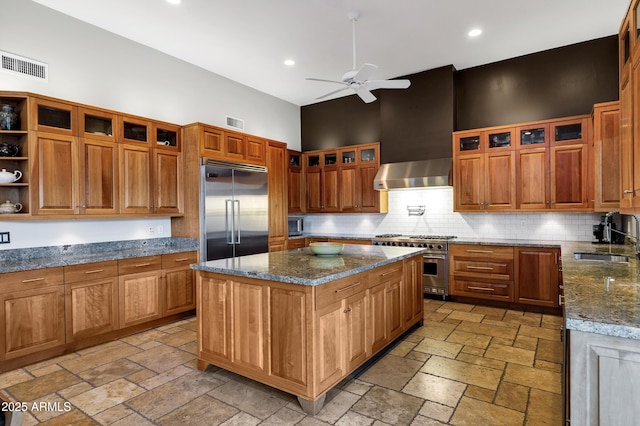 kitchen featuring visible vents, premium appliances, range hood, stone tile floors, and a sink