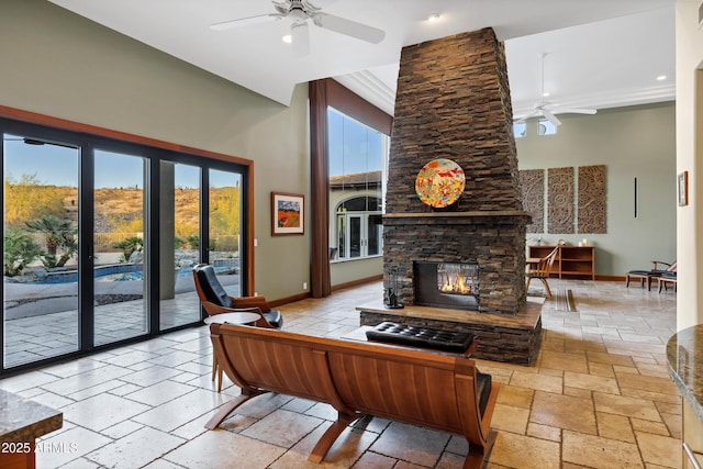living room with a stone fireplace, stone tile flooring, baseboards, and a ceiling fan