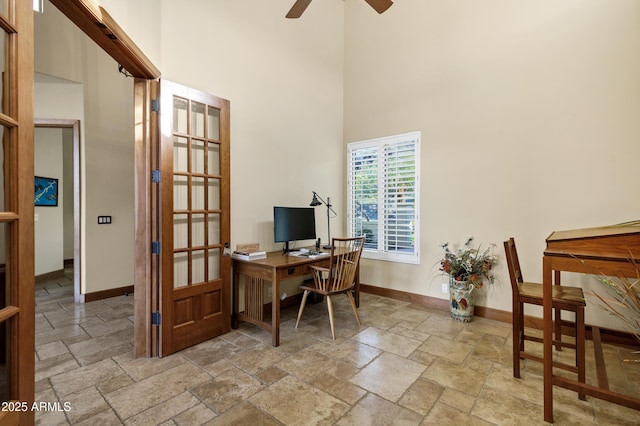 office space with ceiling fan, baseboards, stone tile flooring, and a towering ceiling
